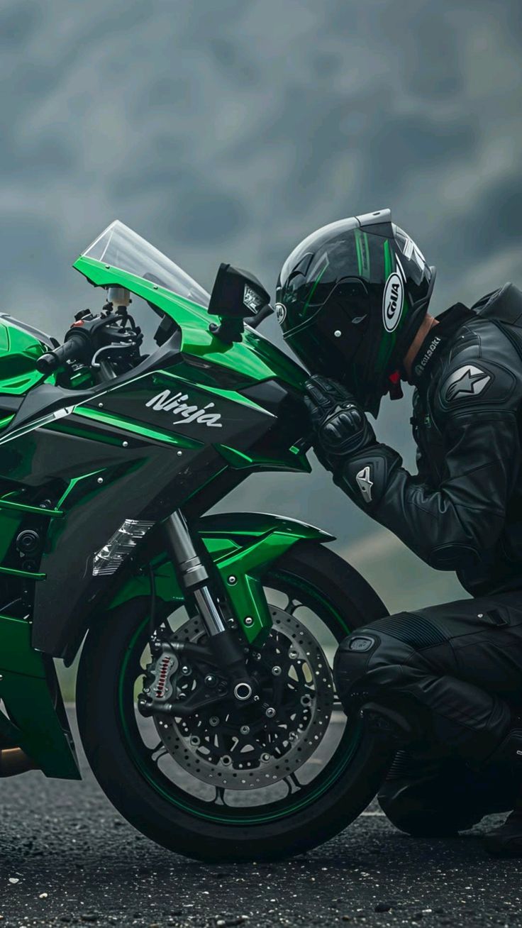 Person wearing a helmet and black jacket next to a green motorcycle with 'Ninja' branding on a cloudy day.