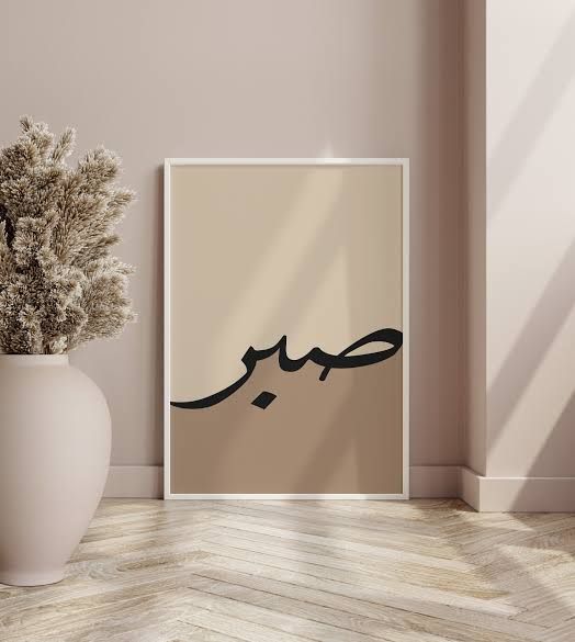 Beige wall with a framed Arabic calligraphy poster and a vase with dried plants.