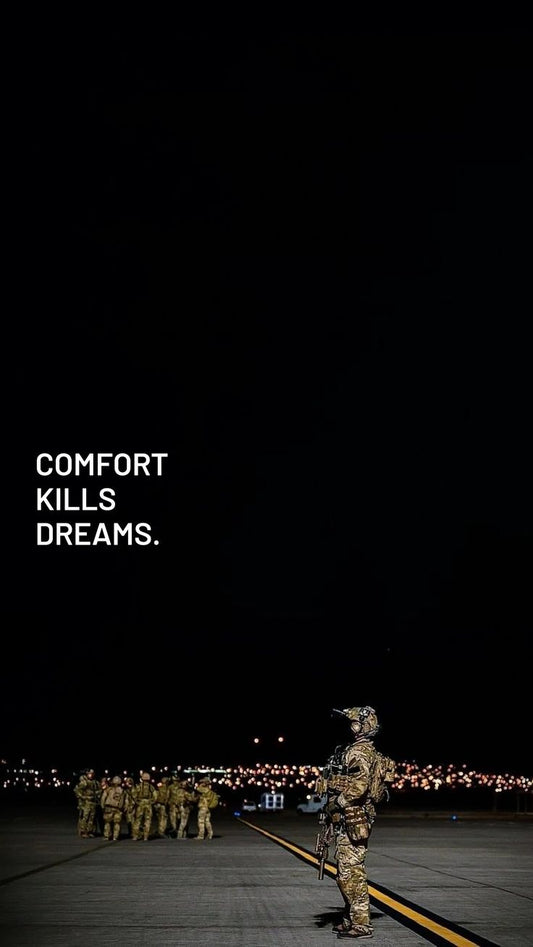 Soldiers in camouflage standing on a runway with a dark sky and text 'COMFORT KILLS DREAMS'.