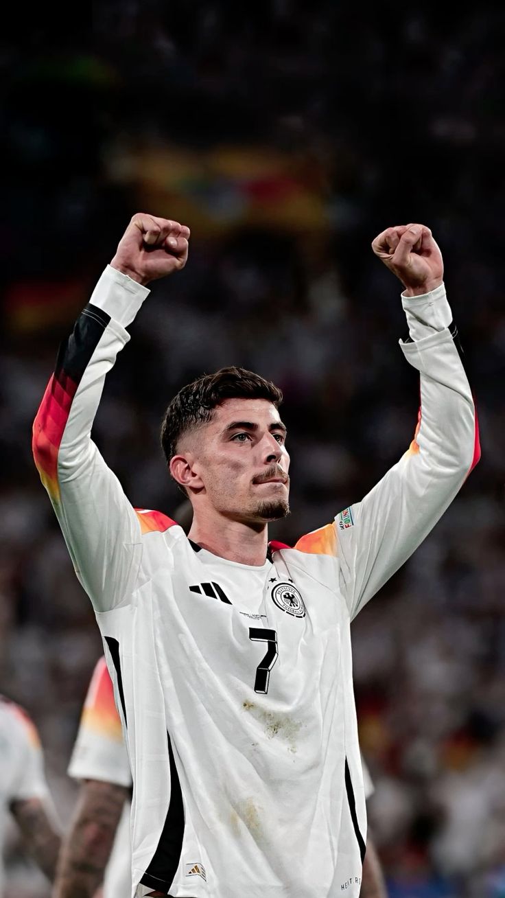 Soccer player in a white jersey with raised arms, celebrating on a field.