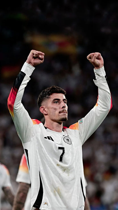 Soccer player in a white jersey with raised arms, celebrating on a field.